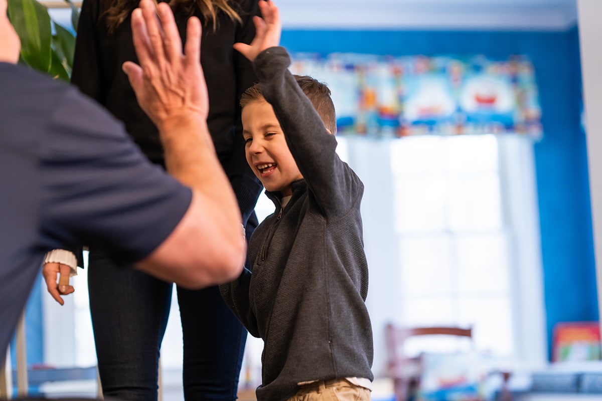 Young child giving high-five to adult in bright blue dental office setting.