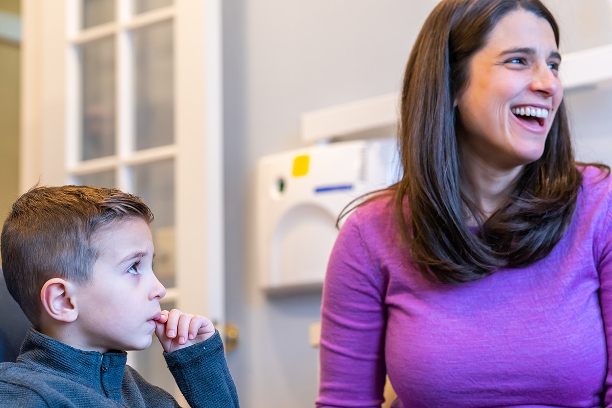 Woman and young boy smiling together in bright dental office setting.