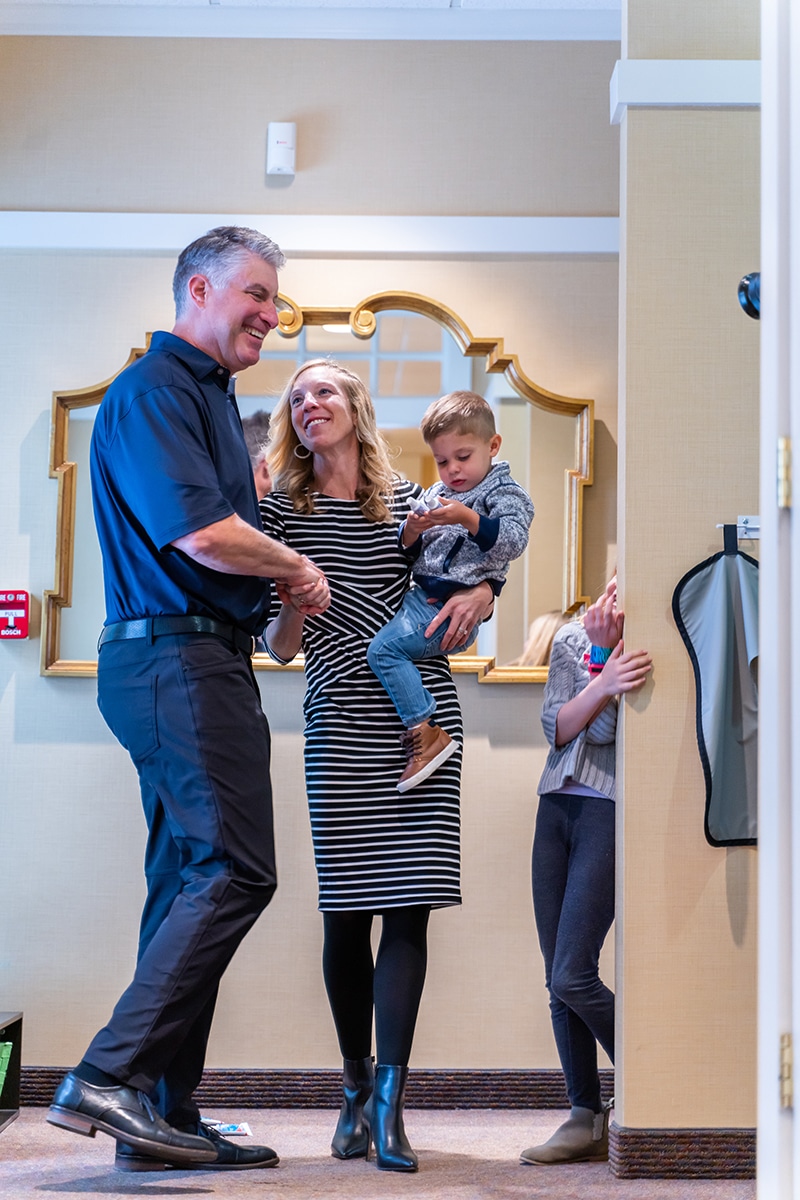 Man in blue uniform smiles with woman and two children in dental office hallway.