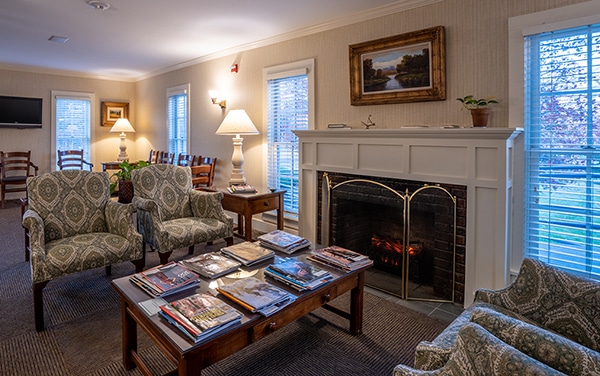 Elegant waiting room with fireplace, upholstered seating, and reading materials.