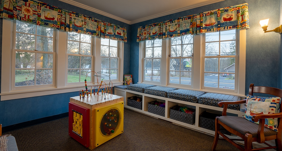 Bright, colorful children's playroom with window seating, toys, and activity cube at dental office.