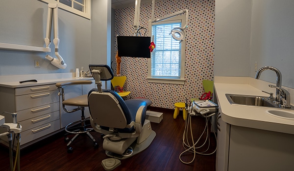 Modern dental operatory with patient chair, overhead monitor, equipment, and sink at Pittsford Family Dental.