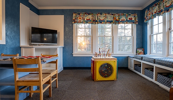 Bright children's playroom with blue walls, wooden furniture, games, and large windows.
