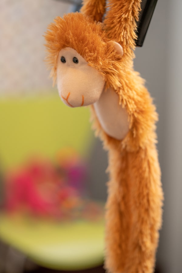 Plush orange monkey toy hanging against blurred colorful background in dental office setting.