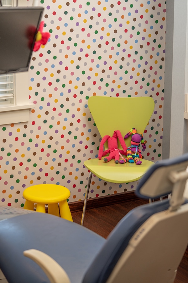 Colorful pediatric dental office waiting room with polka dot wallpaper, yellow chair, and children's toys.