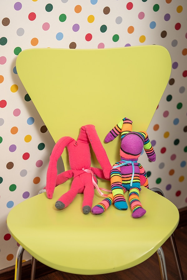 Colorful plush toys sitting on bright yellow chair against polka dot wall.