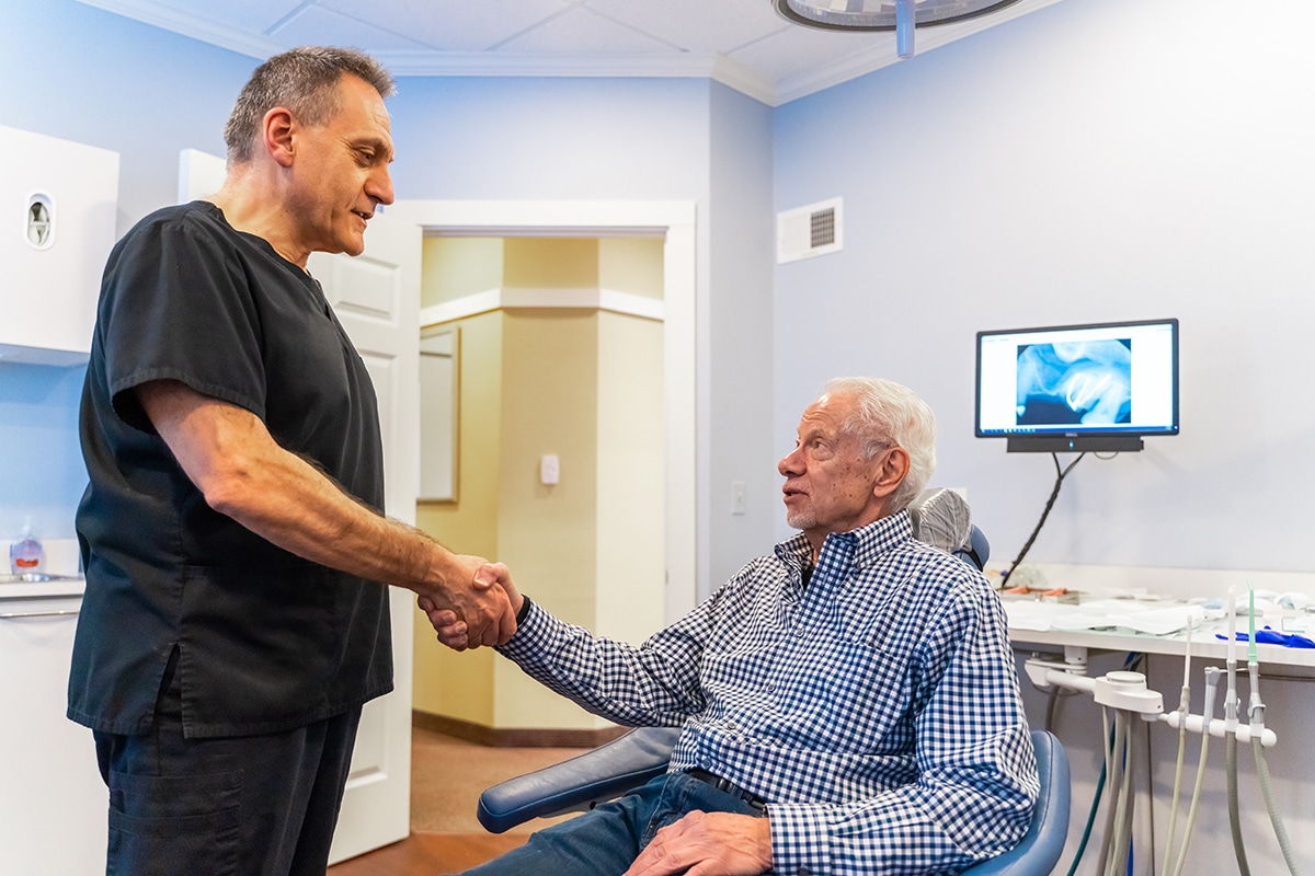 Dentist shaking hands with senior patient in dental office treatment room.
