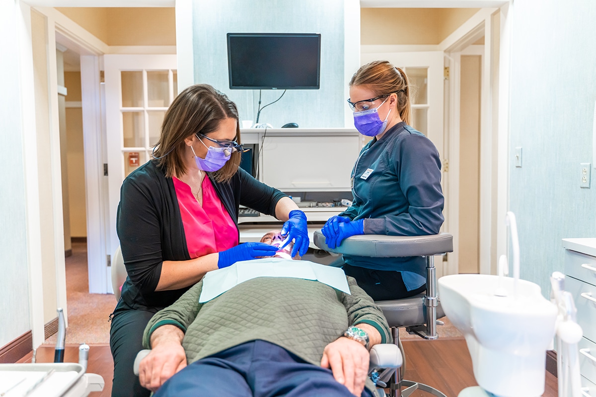 Two dental professionals examine a patient in a modern dental treatment room.