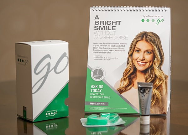 Opalescence Go teeth whitening product display with packaging and instructional calendar on tan background.