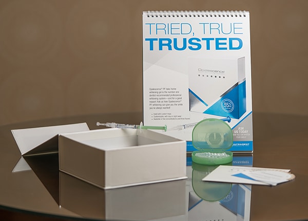 Dental product packaging and white box displayed on reflective surface with brown background.