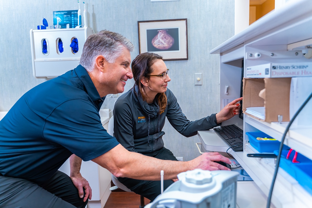 Two dental professionals reviewing computer data in a modern dental office treatment room.