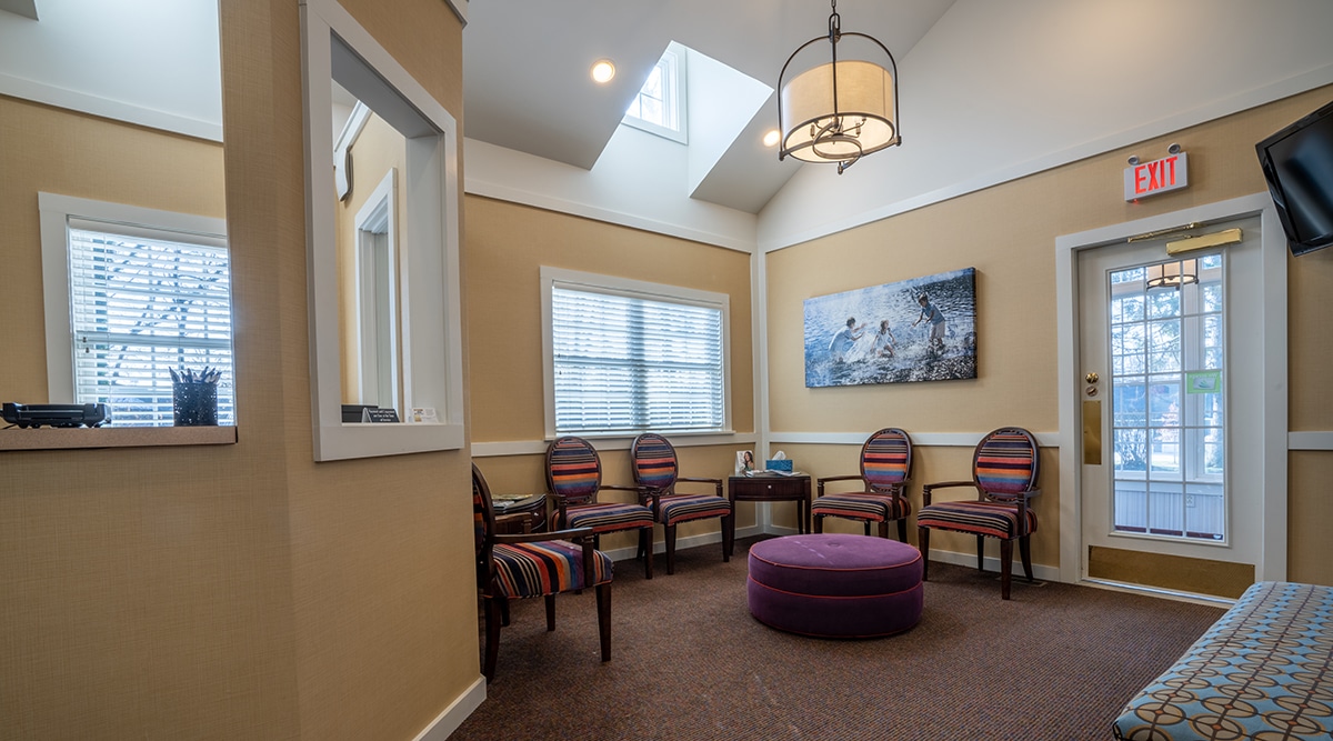 Bright, welcoming dental waiting room with striped chairs, purple ottoman, and natural skylight.