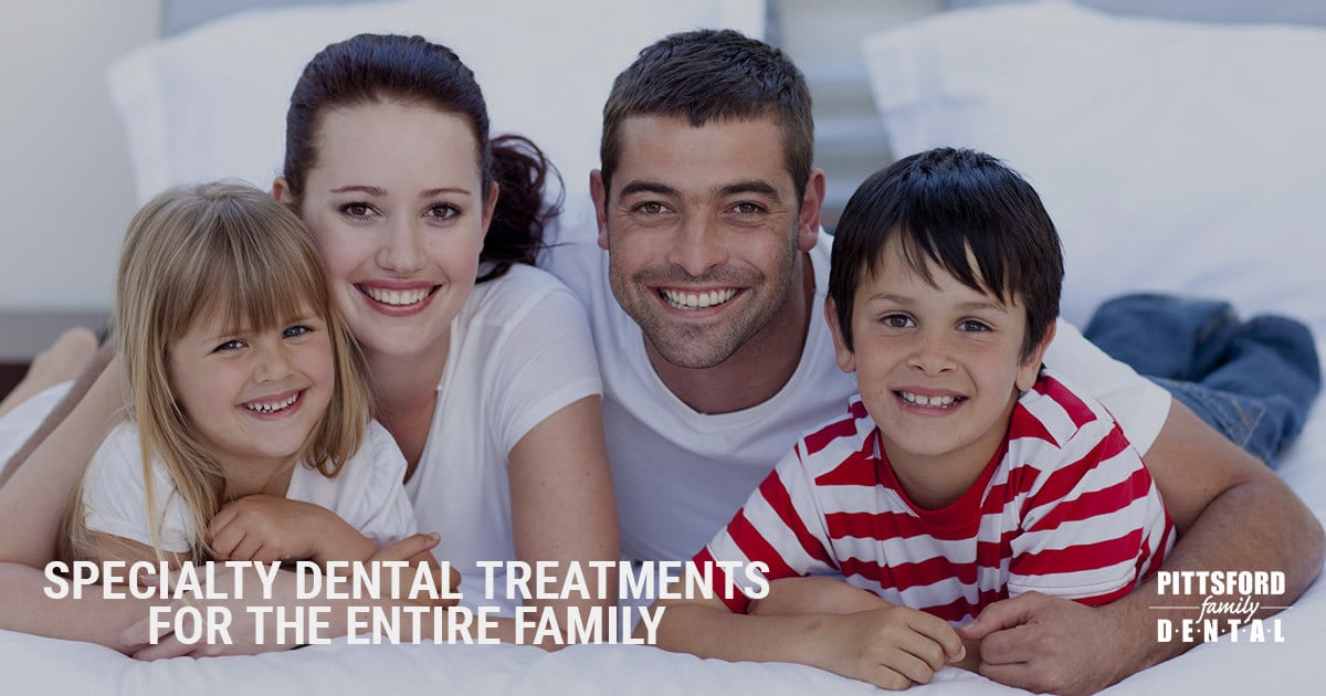 Happy family of four smiling together on bed in dental clinic setting.
