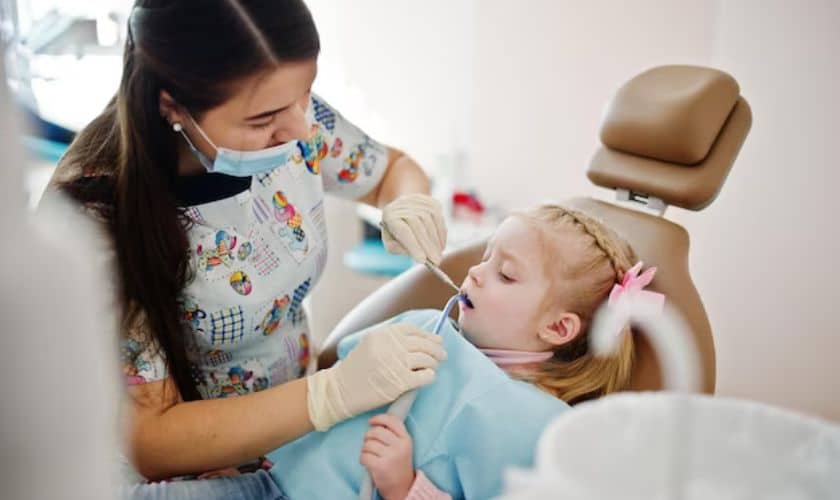 Pediatric dentist examining young child's teeth in dental chair during checkup.
