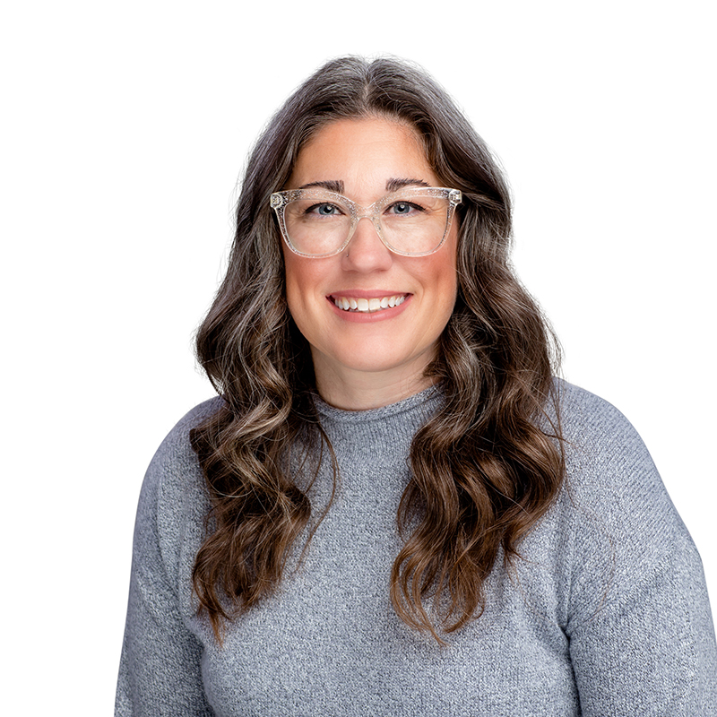 Woman wearing glasses and gray sweater smiling at camera in professional headshot.