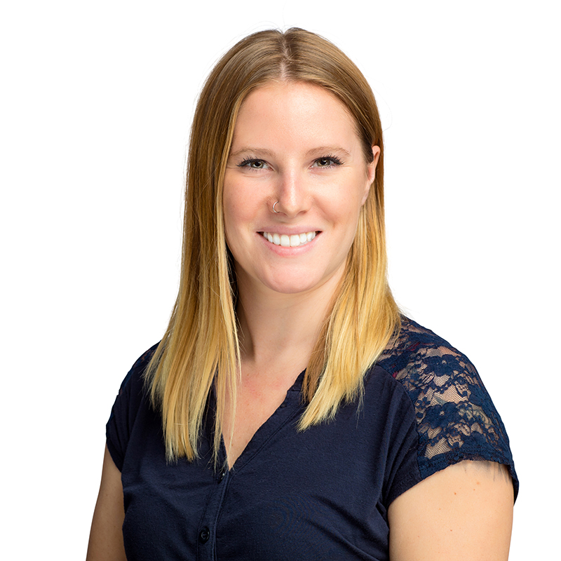 Professional headshot of smiling woman with reddish-blonde hair wearing navy lace blouse against white background.