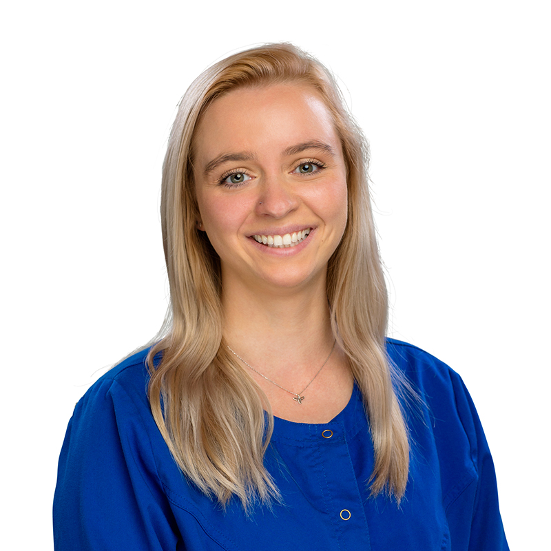Professional headshot of smiling woman in blue scrubs against white background at dental office.