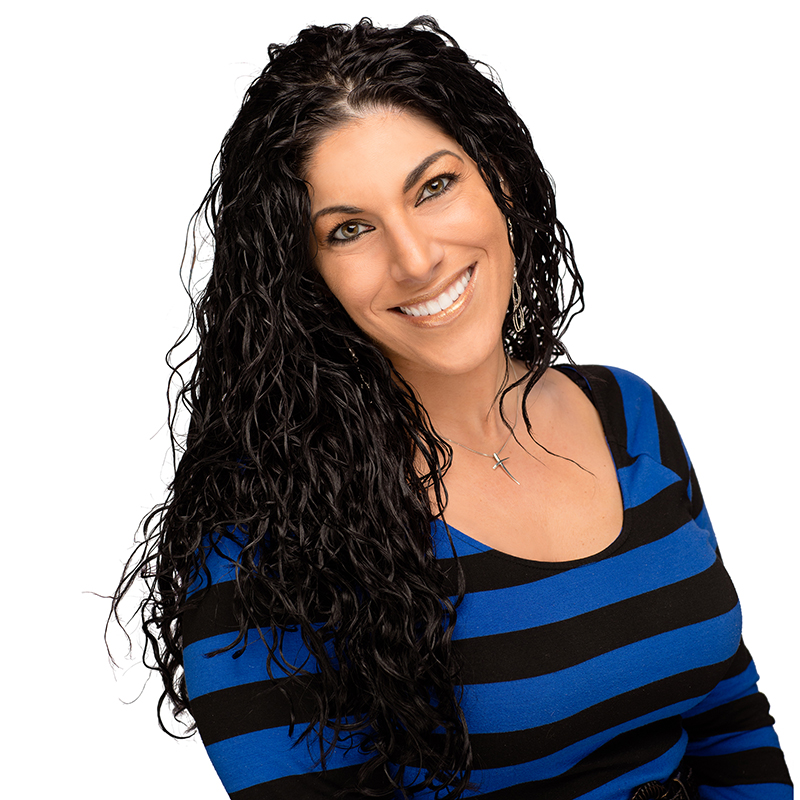 Woman with long black curly hair smiling at camera wearing blue and black striped top against white background.