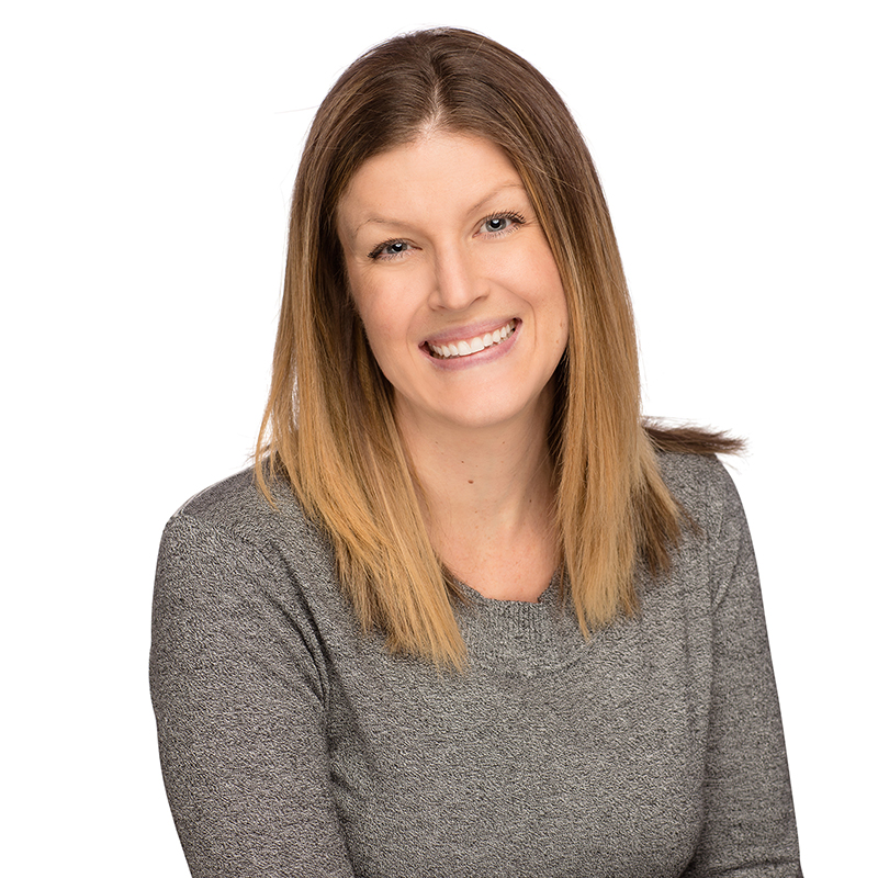 Professional headshot of smiling woman in gray top against white background for dental practice.