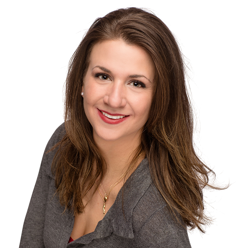 Professional headshot of a woman in gray blazer smiling at camera against white background.