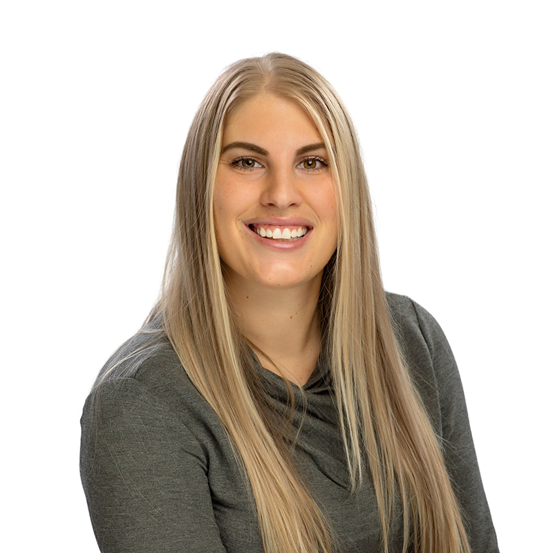 Professional headshot of smiling woman in gray shirt against white background, dental practice staff photo.