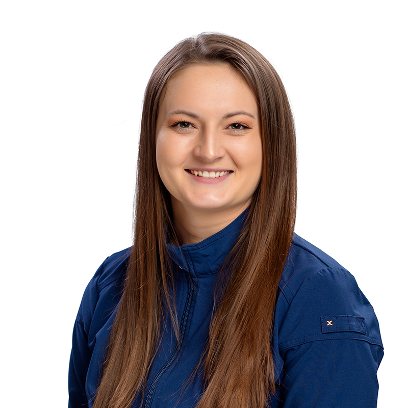 Professional headshot of smiling woman in blue dental scrubs against white background.