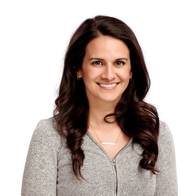 Professional headshot of smiling woman in gray cardigan against white background.