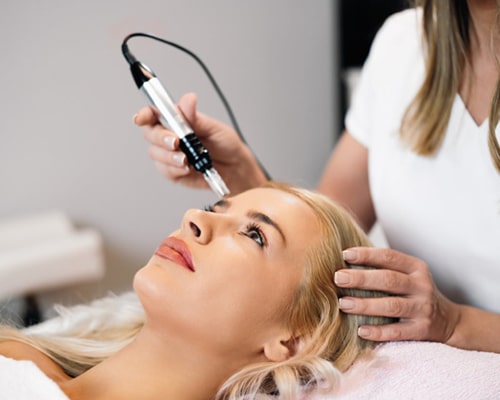 Dental professional performing ultrasonic scaling treatment on patient's face during cosmetic procedure.
