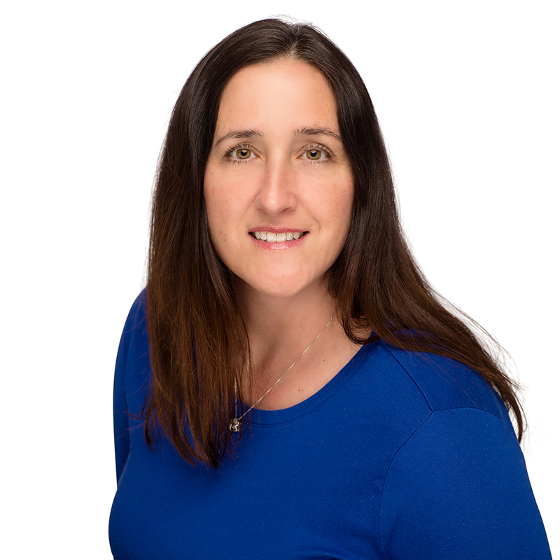 Professional headshot of woman with long dark hair wearing blue shirt against white background.