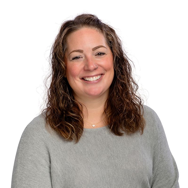 Professional headshot of smiling woman in gray top against white background, dental practice staff portrait.