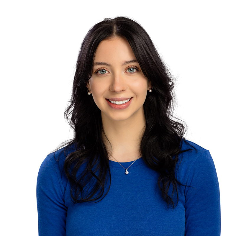 Professional headshot of smiling woman in blue shirt against white background, dental office staff portrait.
