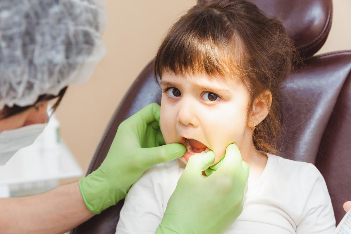 Young girl at dental appointment, dentist in green gloves examining her teeth in office.