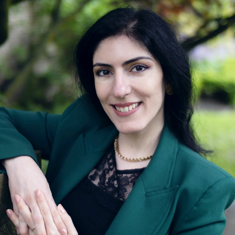 Professional woman in green blazer smiling outdoors in garden setting.